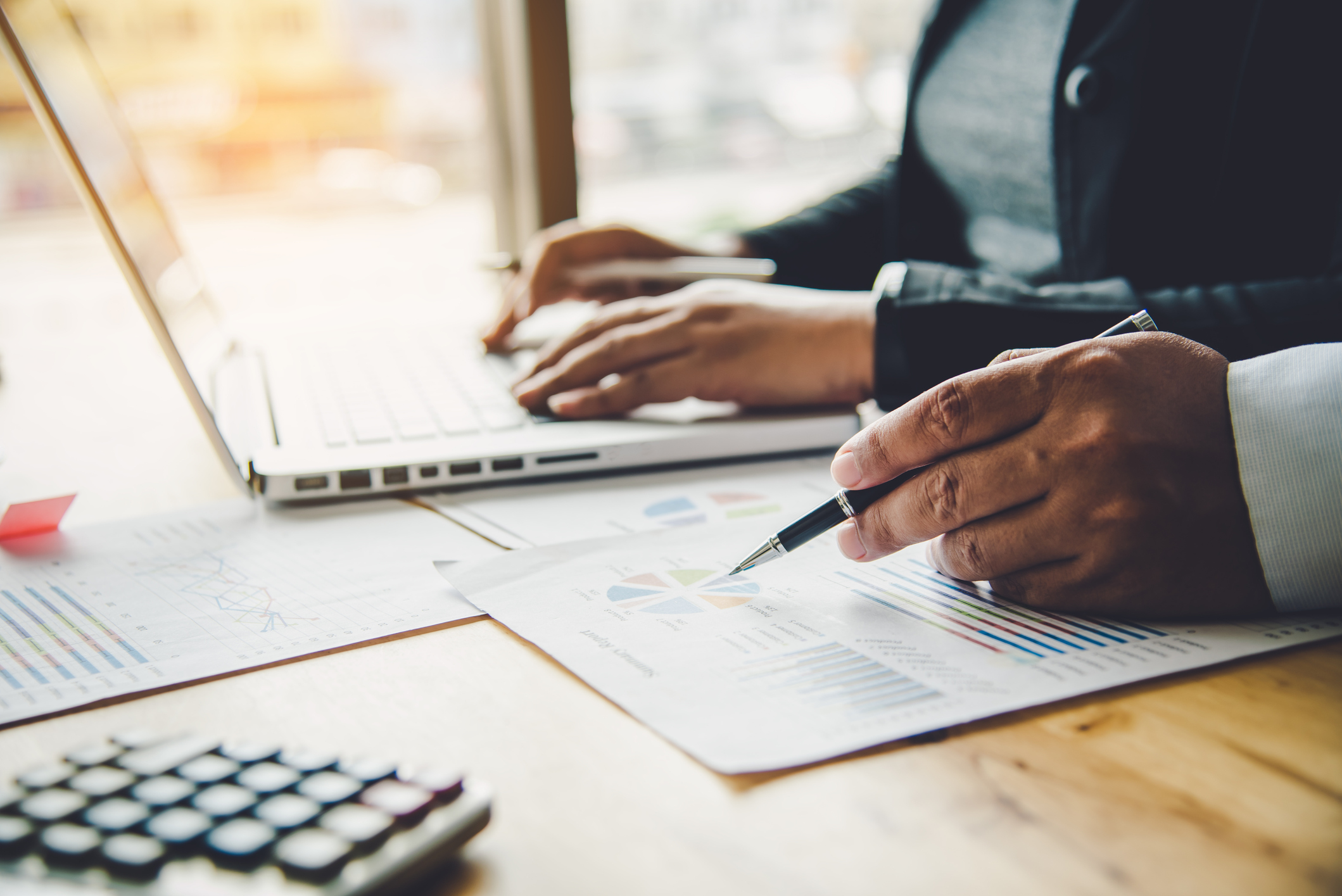 Two professionals review financial charts and graphs on printed documents while working on a laptop, symbolizing personalized banking services, financial planning, and business solutions.